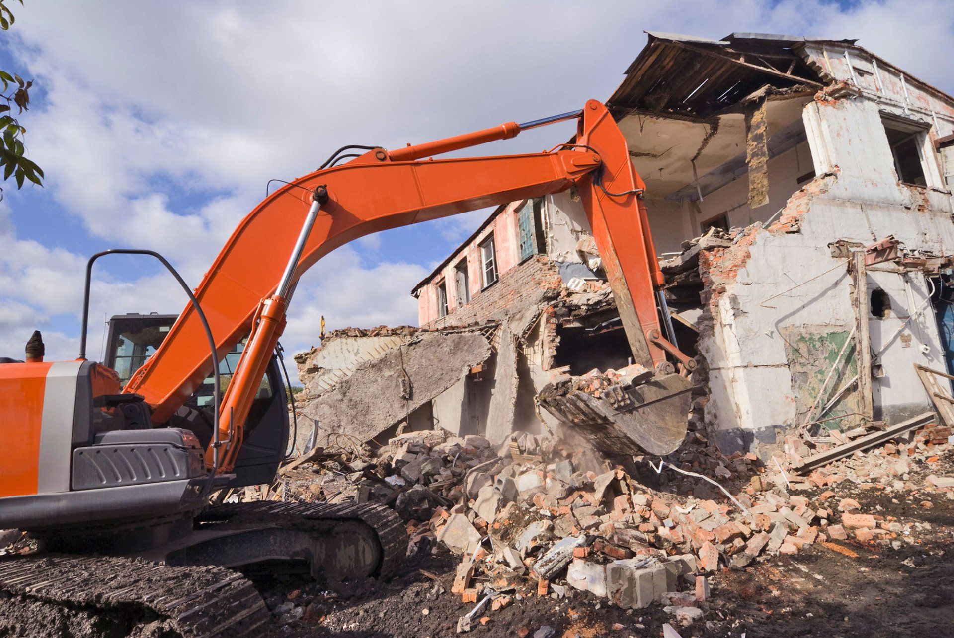 An orange excavator pulling down the brick walls of an old building