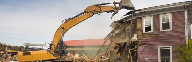 An excavator tearing into a red two-story house