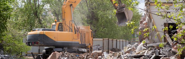 An excavator clearing a demolished building behind a fence